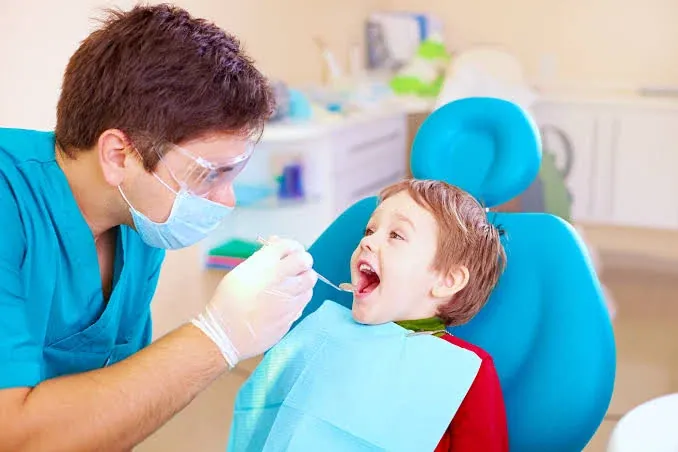 Young boy in a blue dental chair having his teeth checked by a dentist wearing gloves and a mask
